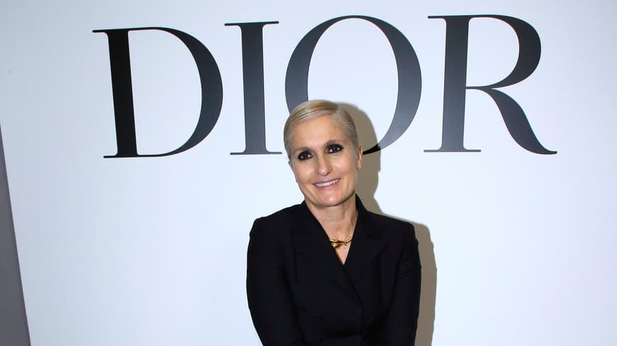 Maria Grazia Chiuri: Alles über die erste weibliche Kreativdirektorin an der Spitze von Dior Maria Grazia Chiuri sitzt vor Dior Schild